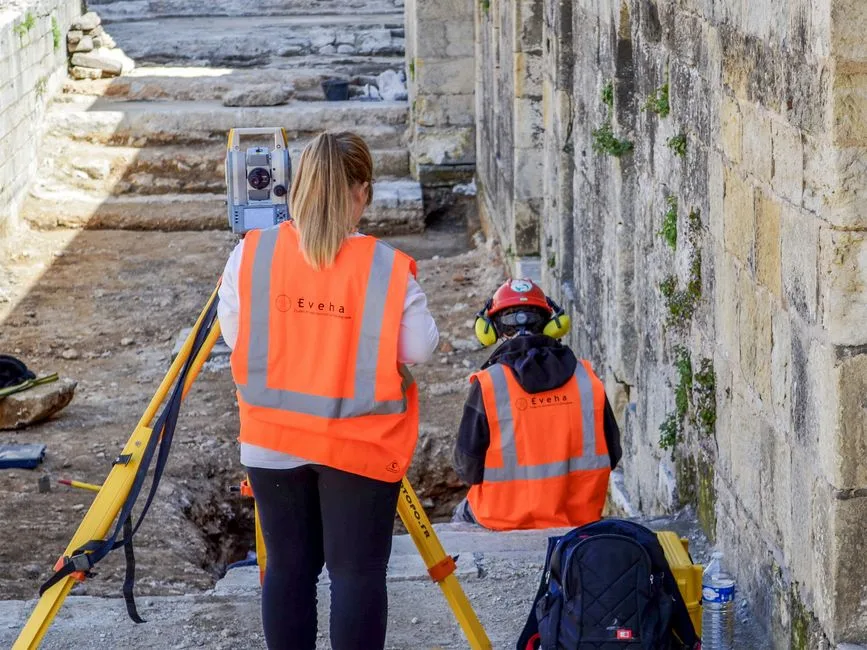 Geólogo revisando mapas de cartografía geológica sobre una mesa de trabajo en campo, con equipos de prospección al fondo